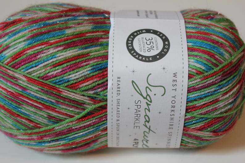 May include: A ball of colorful yarn with red, green, blue, and pink strands, with a label that reads "Signature Sparkle". The yarn contains 75% wool and 35% Bluefaced Leicester. Ideal for knitting and crochet projects.
