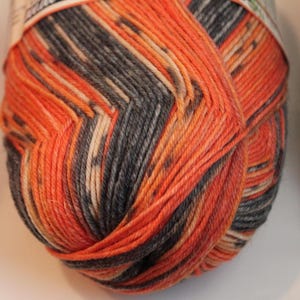 May include: A close-up of a ball of yarn with a blend of colors. The yarn features a mix of orange, gray, and cream hues. The yarn is tightly wound, showcasing the texture and color variations. Ideal for knitting and crochet projects.