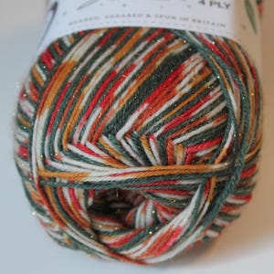 May include: A close-up of a ball of 4-ply yarn with a mix of colors including red, green, white, and gold. The yarn is labeled "Sparkle" and "Bearded, Sheared & Spun in Britain". The yarn is tightly wound and ready for knitting or crocheting projects.