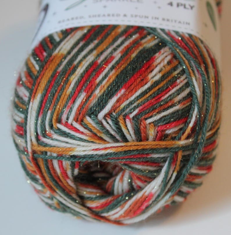May include: A close-up of a ball of 4-ply yarn with a mix of colors including red, green, white, and gold. The yarn is labeled "Sparkle" and "Bearded, Sheared & Spun in Britain". The yarn is tightly wound and ready for knitting or crocheting projects.
