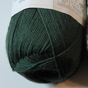 May include: A close-up of a ball of dark green yarn. The yarn is tightly wound and appears soft. The label shows the yarn is 75% wool and 25% nylon. The ball weighs 100g.