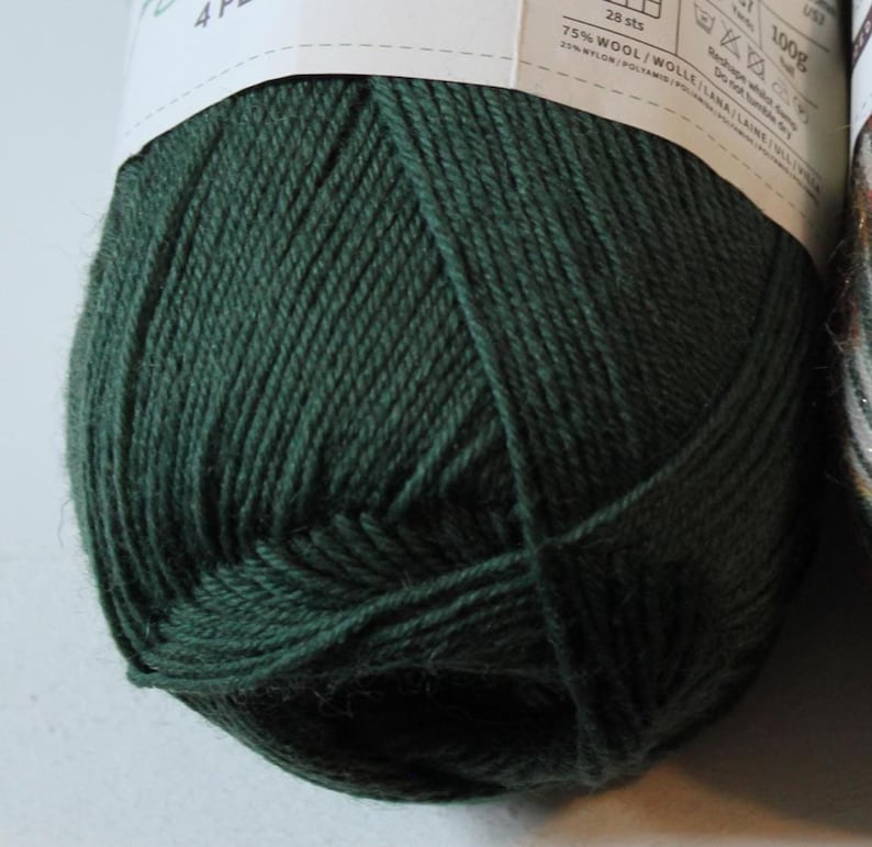 May include: A close-up of a ball of dark green yarn. The yarn is tightly wound and appears soft. The label shows the yarn is 75% wool and 25% nylon. The ball weighs 100g.