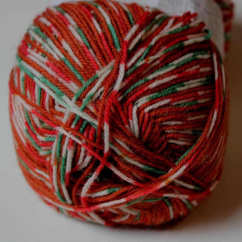 May include: A ball of colorful yarn with a mix of orange, red, white, green, and pink threads. The yarn is tightly wound, showcasing the various colors and textures. Ideal for knitting or crocheting projects.