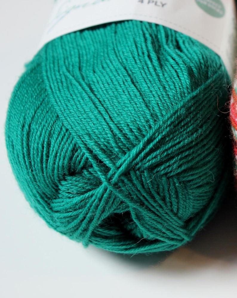 May include: Close-up of a ball of teal green yarn. The yarn is tightly wound, showing the individual strands. The label at the top indicates it is 4-ply yarn. The yarn is a solid, vibrant color, suitable for knitting or crocheting projects.