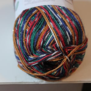 May include: A ball of colorful yarn with strands of red, green, blue, gold, and white. The yarn has a slight shimmer and is tightly wound. The yarn is likely used for knitting or crocheting projects.