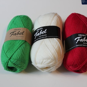 May include: Three skeins of Drops Fabel yarn in green, white, and red. Each skein features a paper band with the text Drops Fabel Uni Colour. The yarn is wound into an oval shape, showcasing a smooth texture and consistent solid coloring.