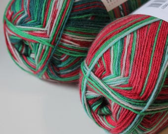 May include: Close-up of two balls of yarn in shades of red, green, white, and light blue. The yarn is tightly wound, showing the different colored strands. The yarn is likely for knitting or crocheting projects.