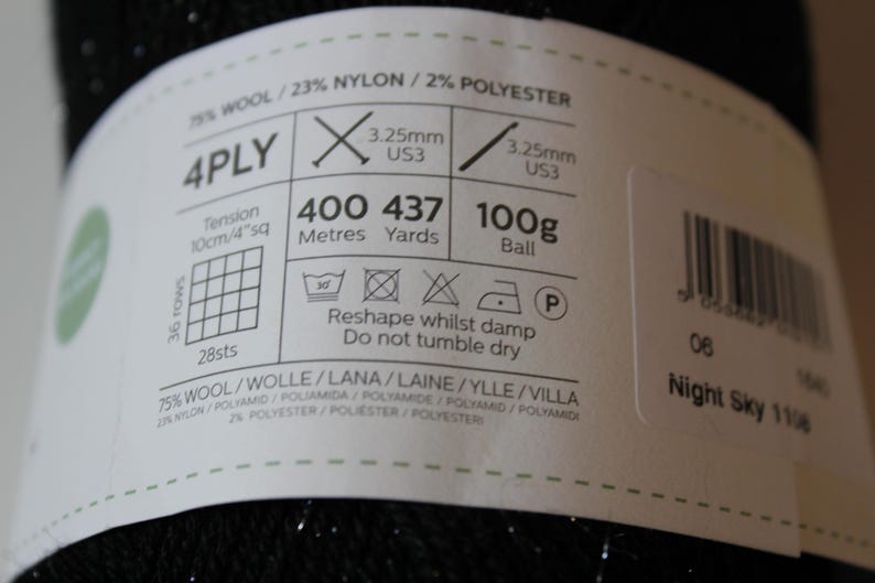 May include: A label wrapped around a ball of black yarn. The label indicates the yarn is 4-ply, 75% wool, and 23% nylon. It includes knitting needle size, 400 meters of yarn, and care instructions. The text "Night Sky 1108" is also visible.