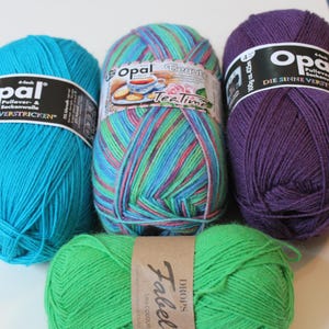 May include: A collection of colorful yarn skeins. The assortment includes teal, multicolored, and purple Opal brand yarns, along with a green Drops Fabel yarn. Each skein is tightly wound, showcasing the texture and color variations.