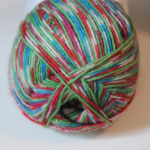 May include: A close-up of a ball of yarn with a colorful mix of red, green, blue, pink, and white threads. The yarn has a sparkly, metallic thread woven throughout, adding a touch of shimmer. The yarn is tightly wound.