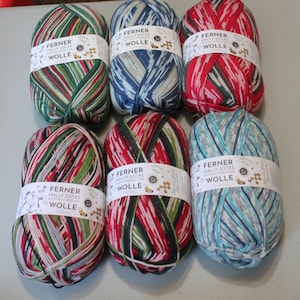 May include: Six balls of yarn in various colors, including red, green, blue, and white. Each ball has a label that reads "Ferner Mally Socks Weihnachts Edition Wolle".