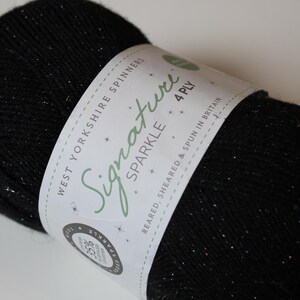 May include: A ball of black yarn with silver sparkle flecks. The yarn is wrapped with a white label that reads "Signature Sparkle 4 Ply" and "West Yorkshire Spinners". The yarn is likely used for knitting or crocheting projects.