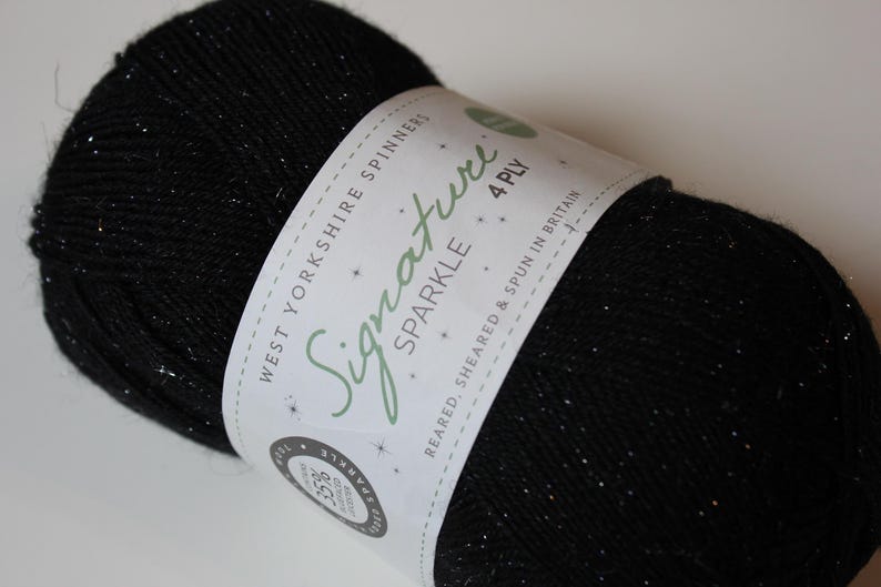 May include: A ball of black yarn with silver sparkle flecks. The yarn is wrapped with a white label that reads "Signature Sparkle 4 Ply" and "West Yorkshire Spinners". The yarn is likely used for knitting or crocheting projects.