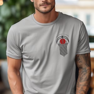 May include: A grey t-shirt with a black and red graphic design on the front. The graphic features a stylised sun with the text "Per Aspera Ad Astra" around it.