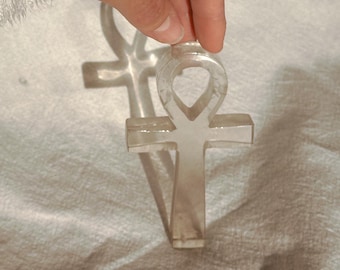 May include: A clear, translucent ankh symbol crafted with a smooth, polished finish. The object features the traditional cross shape with a looped top, reflecting light through its semi-transparent material, showcasing a clean and simple design.