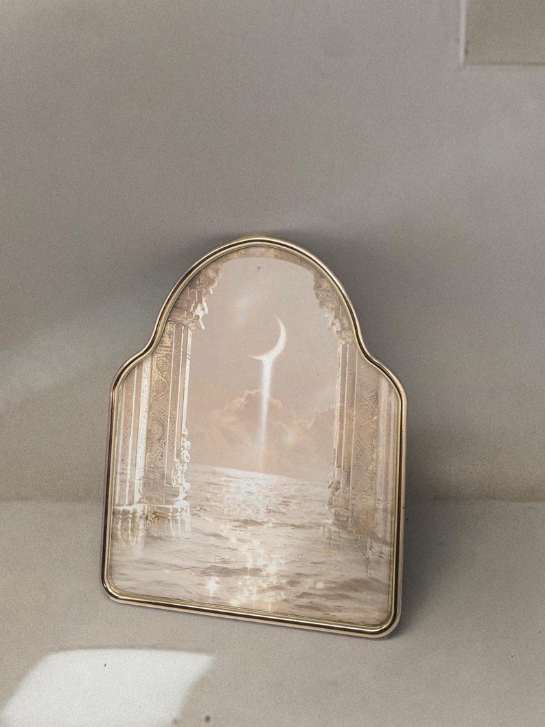 K&ouml;nnte beinhalten: Ein silberfarbener Bilderrahmen mit gew&ouml;lbtem Oberteil. Das Bild zeigt eine Himmelszene mit einem Halbmond, S&auml;ulen und Wasser. Der Rahmen hat einen dekorativen Rand und eine Vintage-&Auml;sthetik.
