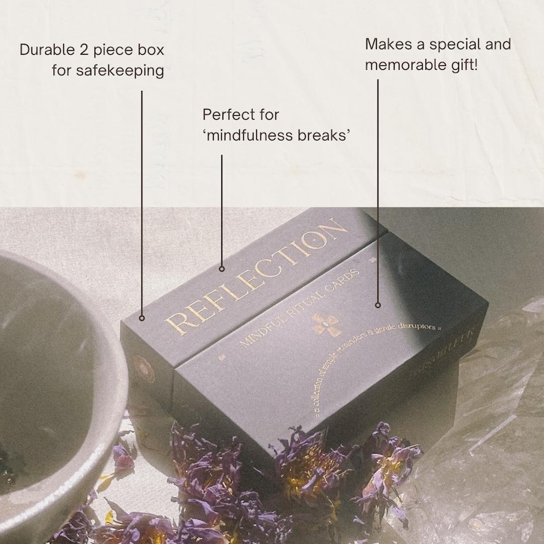 Op de afbeelding: Een zwarte rechthoekige tweedelige doos met de gouden tekst REFLECTION MINDFUL RITUAL CARDS. De doos bevat een klein gouden kruissymbool en de tekst a collection of simple mindful gentle disruptors. De doos staat in de buurt van een kom.