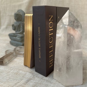 an affirmation mindfulness deck is on its side with golden foil and a clear quartz