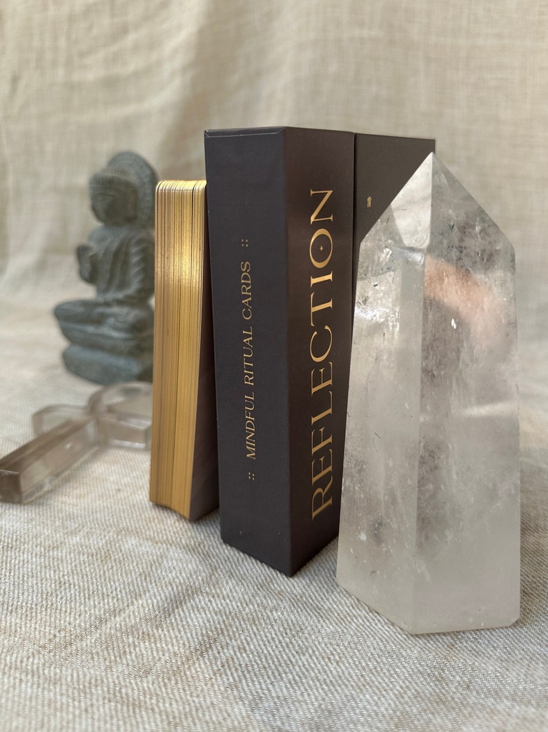 an affirmation mindfulness deck is on its side with golden foil and a clear quartz