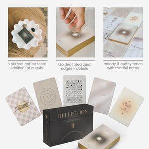 Op de afbeelding: Een set Reflection orakelkaarten met een zwarte doos met gouden tekst, vergezeld van verschillende kaarten in aardetinten met minimalistische afbeeldingen en inspirerende teksten. De kaarten hebben goudfolie randen en zijn in diverse lay-outs gepresenteerd.