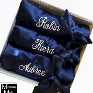 May include: Navy blue satin robes with embroidered names "Robin", "Kiera", and "Aubree" in a gift box. Each robe has a matching sash tied in a bow. The box also has the text "Memories Made Apparel" and "EMBROIDERY".