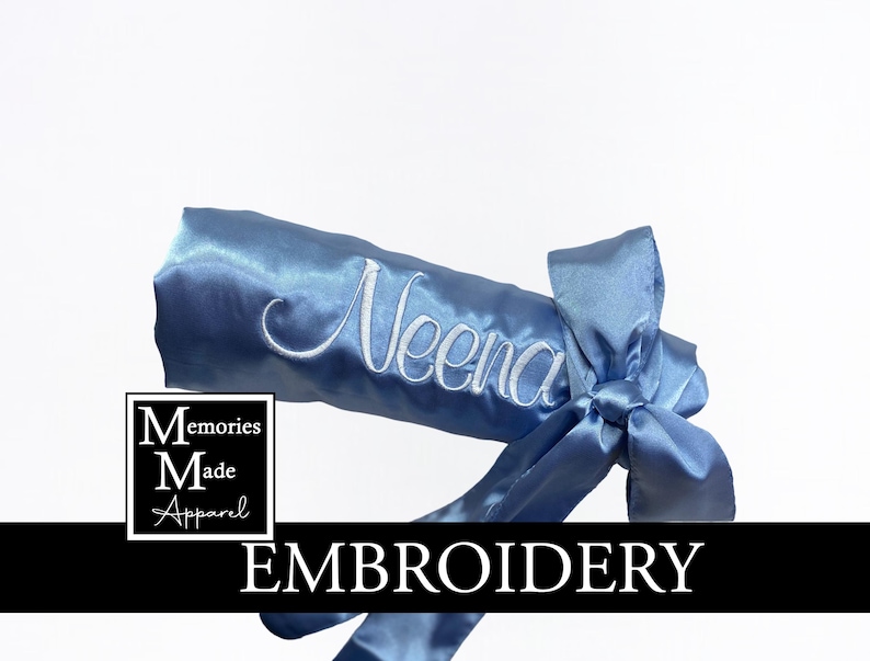 May include: A light blue satin sash embroidered with the name "Neena" in white script. The sash is tied in a bow and features the text "EMBROIDERY" in a black banner. The logo "Memories Made Apparel" is in a white square.