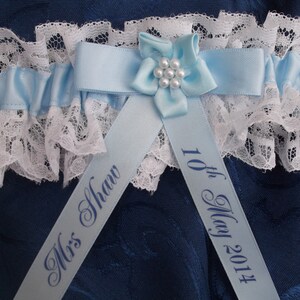 K&ouml;nnte beinhalten: Ein blaues und wei&szlig;es Strumpfband mit einem blauen Satinband und einer wei&szlig;en Spitzenborte. Das Band ist mit dem Text "Mrs. Shaw" und "10th May 2014" personalisiert.