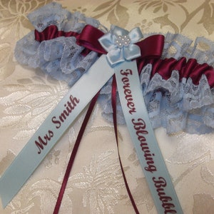 May include: A blue and burgundy garter with lace trim and two satin ribbons. One ribbon is personalized with "Mrs. Smith" and the other with "Forever Blowing Bubbles".