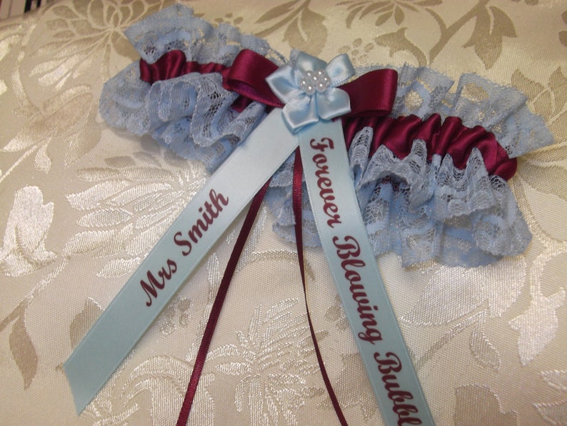 May include: A blue and burgundy garter with lace trim and two satin ribbons. One ribbon is personalized with "Mrs. Smith" and the other with "Forever Blowing Bubbles".