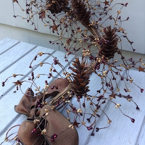 May include: A brown and beige twig wreath with small red berries and gold stars. The wreath is tied with a brown ribbon bow.