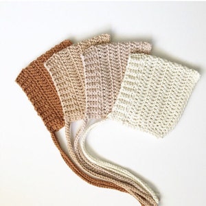 May include: Four crocheted baby bonnets in shades of brown, beige, and white. The bonnets have long ties.