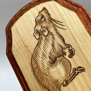 K&ouml;nnte beinhalten: Ein mit einem Brenneisen gebranntes Design eines Ratten auf einer Holzplatte mit braunem Rand.