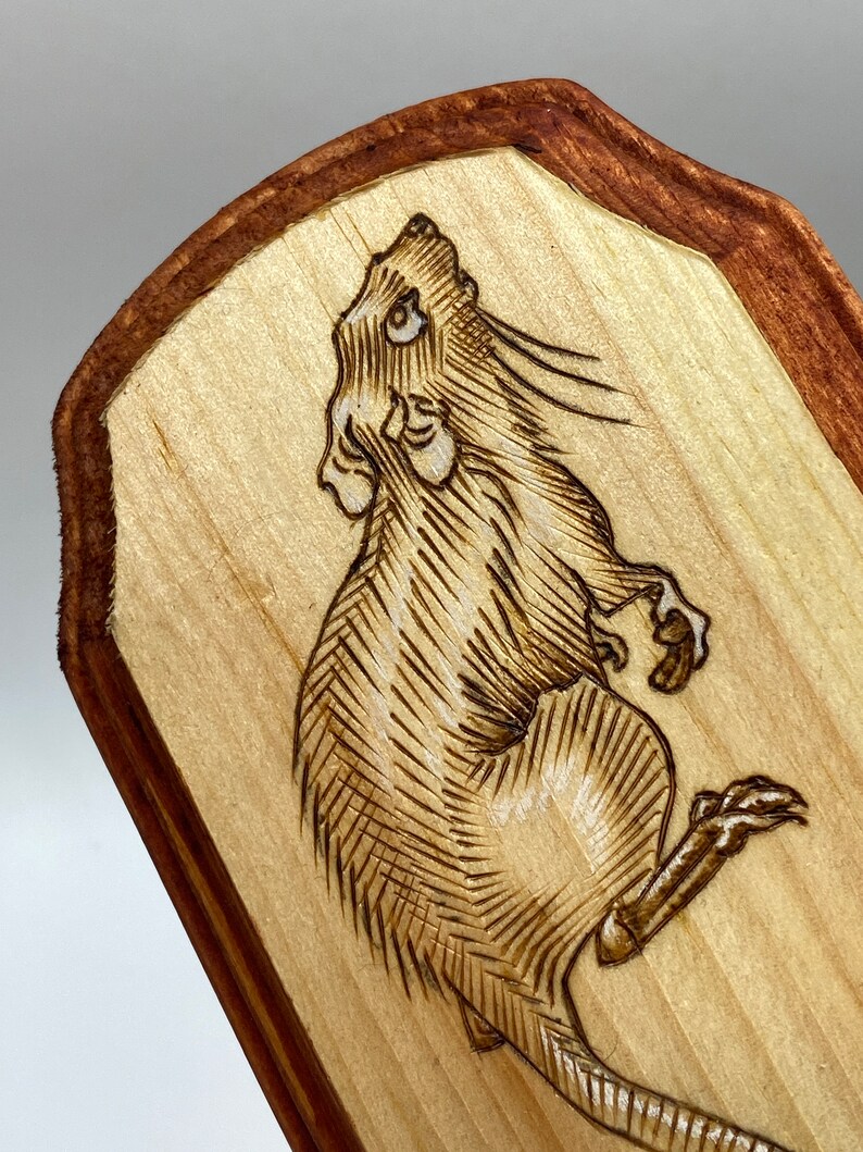 K&ouml;nnte beinhalten: Ein mit einem Brenneisen gebranntes Design eines Ratten auf einer Holzplatte mit braunem Rand.