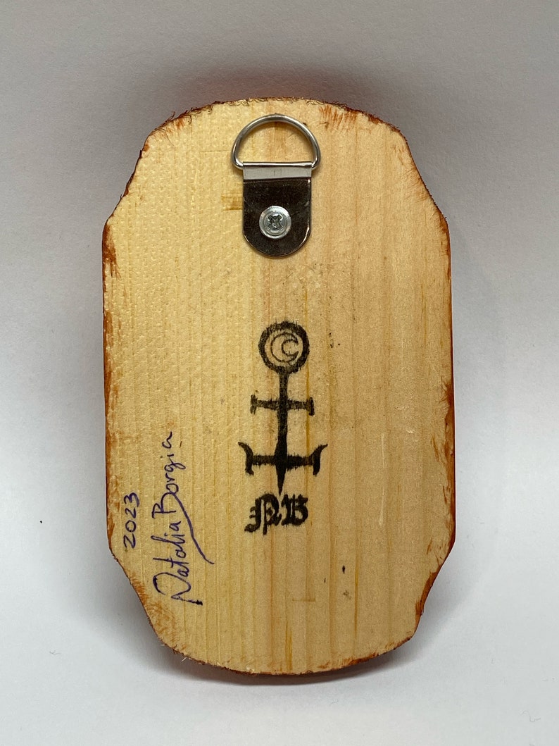 K&ouml;nnte beinhalten: Die R&uuml;ckseite eines Holzgem&auml;ldes mit einem Metall-Aufh&auml;nger. Das Gem&auml;lde ist signiert mit "Natalia Borgia" und datiert mit "2023". Es gibt ein Symbol mit einem Kreuz und den Buchstaben "J.P.B."