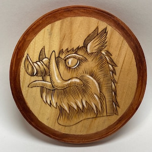 May include: A wooden circular plaque with a brown border and a detailed wood-burned image of a boar's head with a large snout and tusks.