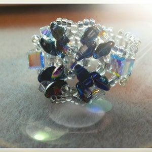 May include: A beaded ring with a flower design made with iridescent blue and clear beads.