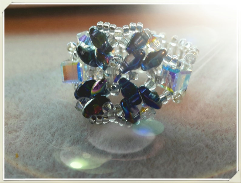 May include: A beaded ring with a flower design made with iridescent blue and clear beads.