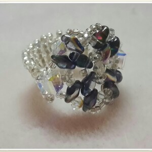 May include: A silver ring with black and iridescent beads, woven together in a delicate pattern.