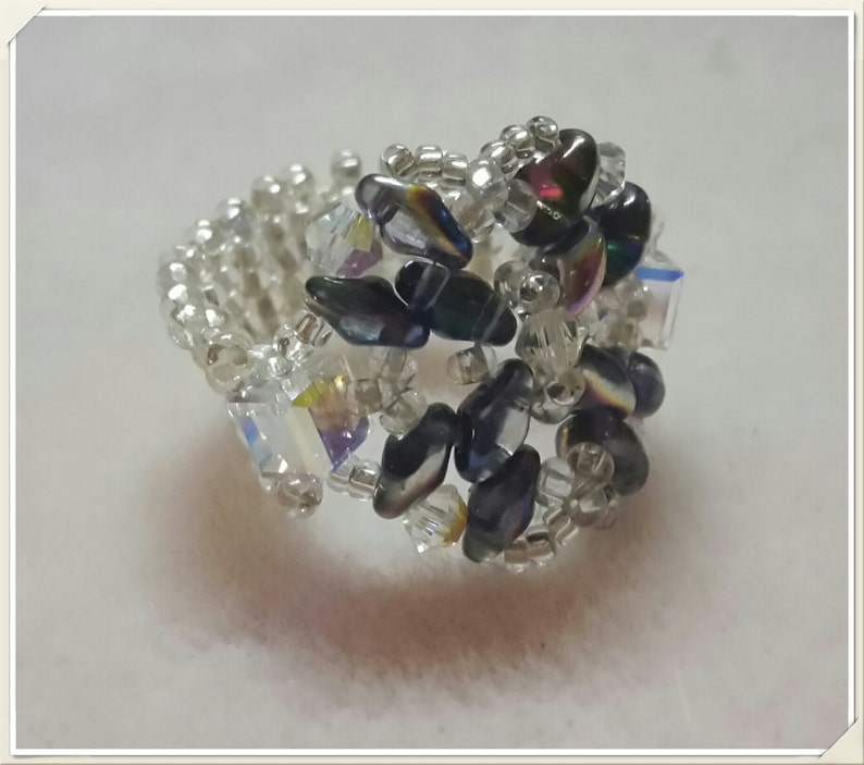 May include: A silver ring with black and iridescent beads, woven together in a delicate pattern.