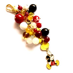 Può includere: Un portachiavi dorato con un ciondolo di Topolino e un gruppo di perline colorate. Le perline sono rosse, bianche, nere, gialle e trasparenti.