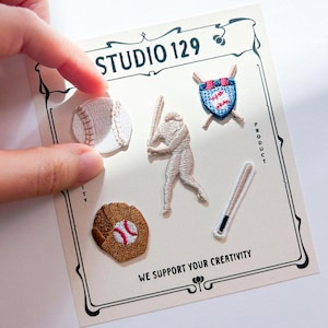 Può includere: Un set di sei toppe ricamate da stirare con disegni a tema baseball. Le toppe includono una palla da baseball, un guanto da baseball, una mazza da baseball, un giocatore di baseball e uno scudo con una palla da baseball all'interno. Le toppe sono su una carta bianca con il testo "STUDIO 129" e "WE SUPPORT YOUR CREATIVITY".