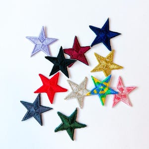 May include: A collection of embroidered star patches in various colors, including red, blue, gold, and green. The patches are arranged on a white background, showcasing their detailed stitching and vibrant hues. These patches are ideal for adding a decorative touch to clothing or accessories.