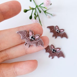 May include: Three brown felt bat appliques with pink ears and black eyes. The bats are approximately 2.5 cm in size.