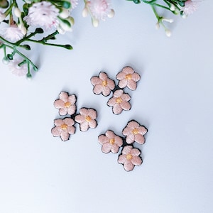 Op de afbeelding: Zes kleine roze geborduurde bloemenpatches met gele centra. De patches bevinden zich op een witte achtergrond.