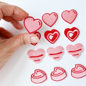 Może przedstawiać: Zestaw 10 haftowanych naszywek w kształcie serca w kolorze różowym i czerwonym. Naszywki są w różnych stylach, w tym pełne serca, serca z białym obramowaniem i serca z białym sercem wewnątrz.