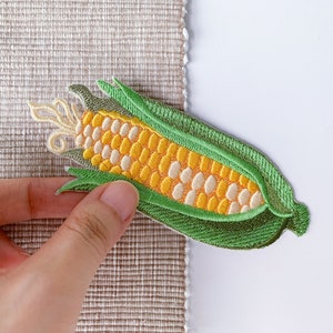May include: An embroidered patch of a corn cob with husks, in green and yellow.
