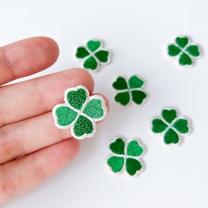 May include: Six green four-leaf clover patches with white outlines. The patches are embroidered and have a slightly raised texture.