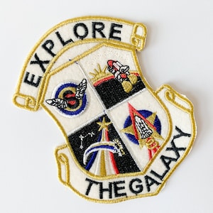 May include: A white embroidered patch with gold trim and the text "Explore the Galaxy". The patch features a crest with four quadrants, each with a different space-themed design.