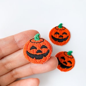 May include: Three orange felt pumpkin patches with embroidered black eyes, noses, and mouths. The pumpkins have green stems.