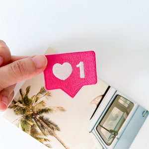May include: A pink heart-shaped notification icon with a white heart and the number "1" embroidered on it.